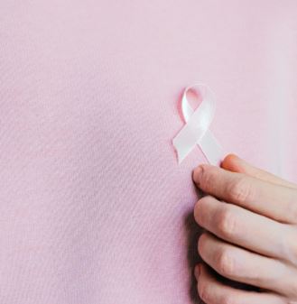 A woman wearing a pink ribbon, pinned to a pink sweater.